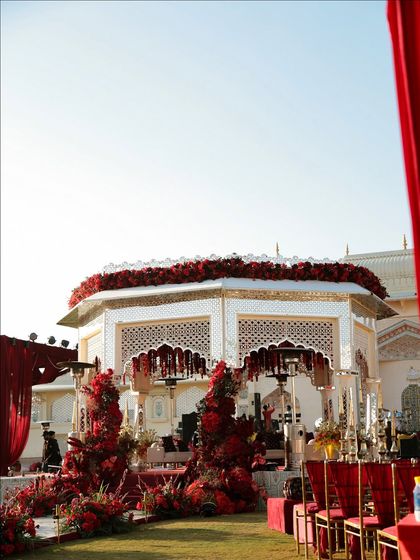 A detailed view of the hexagonal mandap, showcasing the intricate jali work and the rich layer of red roses on top. The design combines traditional Rajasthani motifs with a bold, modern color statement.
