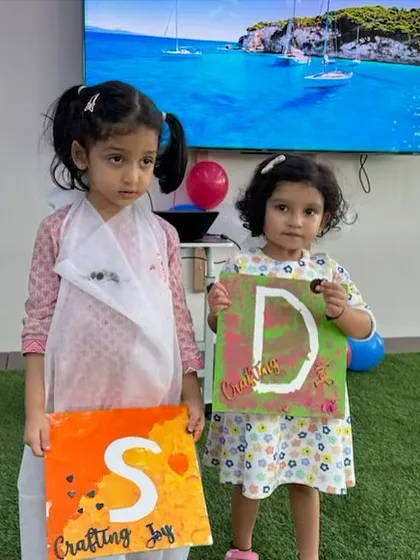 Two young artists proudly displaying their finished initial canvases. We love seeing the unique color choices and personal touches each child adds to their work.