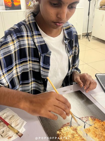 A student works on her gold foil tree painting, learning how to blend a painted background with metallic leafing.