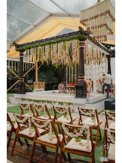 A wide shot of the mandap, showing the seating arrangement and the impressive floral chandelier hanging above. This setup combines traditional structure with grand floral elements.