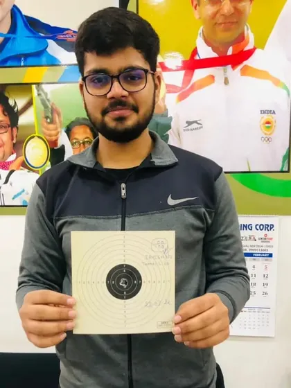 A champion in the making, holding his target card in front of our wall of inspiration, which features photos of national and international shooting icons.