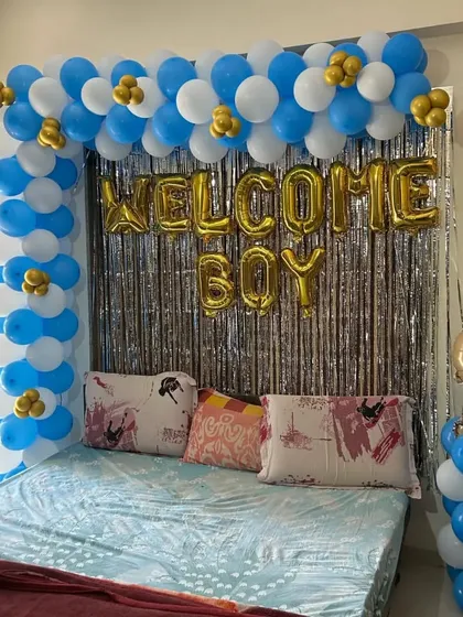 A bedroom setup to welcome a new baby boy, with a blue, white, and gold balloon arch and "Welcome Boy" foil letters.
