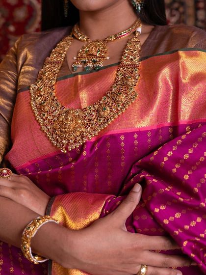 A detailed view of the deep pink Kanchipuram silk saree, highlighting the intricate gold buttis and the heavy temple necklace.
