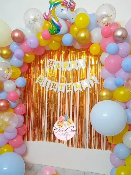 A bright and cheerful unicorn-themed first birthday with a pastel balloon arch against a gold shimmer curtain.