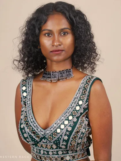 This close-up portrait focuses on the exquisite detail of a Shisha mirror-work blouse. The direct, confident gaze of the model contrasts with the traditional craftsmanship, creating a powerful image for fashion lookbooks or a modeling portfolio.
