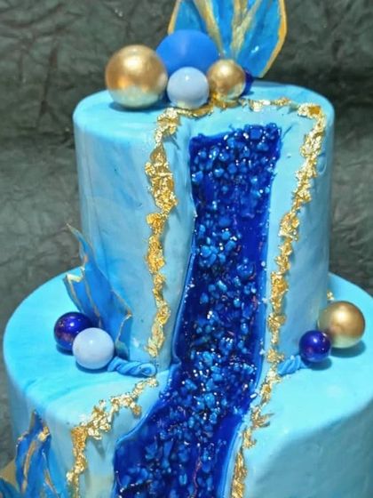 A stunning two-tiered geode cake. The design features a realistic, edible blue crystal formation running through the cake, edged with gold leaf for a luxurious finish.