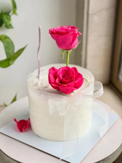 A full view of the pink rose cake, complete with a single candle, ready for a wish to be made. The fallen petal adds a touch of romance.
