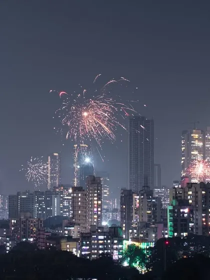A wide shot of the Mumbai skyline during Diwali, with multiple fireworks lighting up the night over the city's countless buildings.