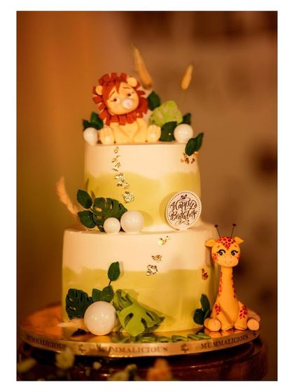 A beautifully crafted two-tier cake for a safari-themed party. It's adorned with adorable, edible figures of a lion and a giraffe, along with delicate leaf details.