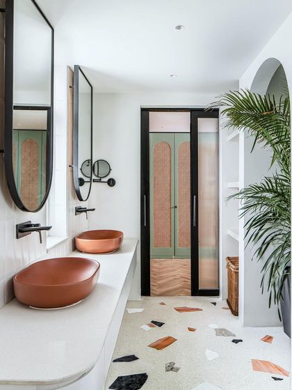 The master bathroom features a custom terrazzo floor, terracotta-colored basins, and a sliding door with cane and fluted glass panels, blending textures and colors beautifully.