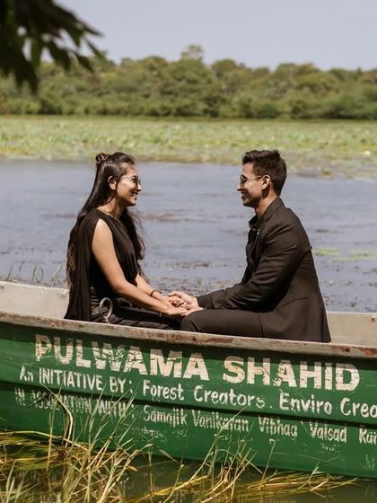 A beautifully framed shot of the couple in the boat, with lush green foliage in the foreground. This composition adds depth and a sense of privacy to their romantic moment.