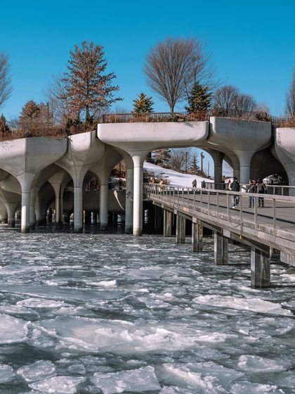 The unique architecture of Little Island park on a cold winter day, with ice floes on the Hudson River. The contrast between the modern structure and the natural ice is striking.