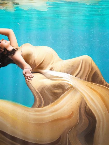 A serene and weightless "underwater" portrait. The golden gown flows beautifully, creating a dreamlike image of the mother-to-be floating peacefully.