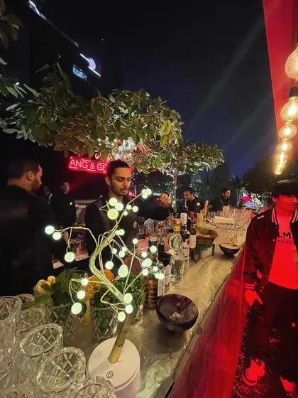 Our team serving guests at an upscale evening event. The setup features warm, ambient lighting from Edison bulbs and decorative light-up trees, creating a sophisticated and inviting atmosphere.