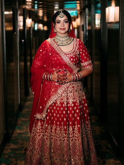 A full-length portrait of the bride in a beautifully lit hallway, her red lehenga radiant against the warm tones.