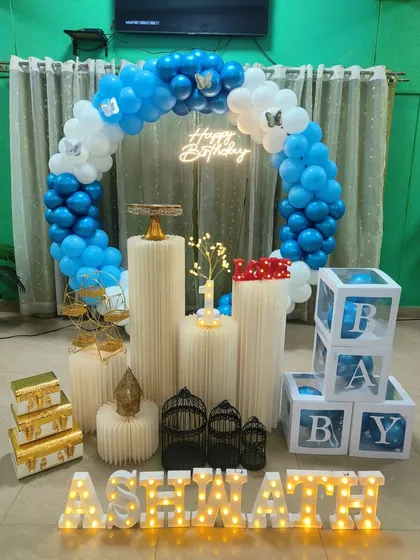 A full view of a blue and white balloon ring setup for a first birthday, including 'B-A-B-Y' blocks, props, and a personalized light-up name.