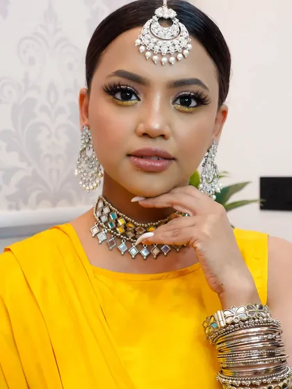 A perfect Haldi look. We created a bright and sunny style with a pop of yellow on the inner corner of the eyes, glossy lips, and sleek hair to go with her yellow outfit and silver jewelry.