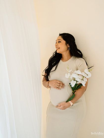 A serene studio portrait, with the mom-to-be holding a bouquet of white orchids. The flowers add a touch of elegance and symbolize new life.