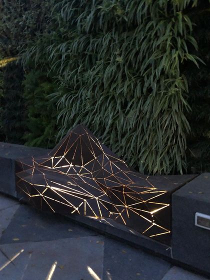 The "Origami" bench, a sculptural piece with illuminated geometric patterns. Set against a living wall, this bench is a stylish and functional work of art that transforms the outdoor seating experience.