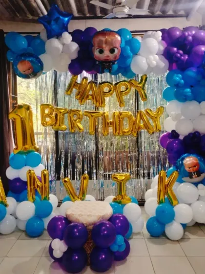 An identical image of the "Boss Baby" themed first birthday party, showcasing the full setup with a tinsel curtain backdrop and a small cake table.