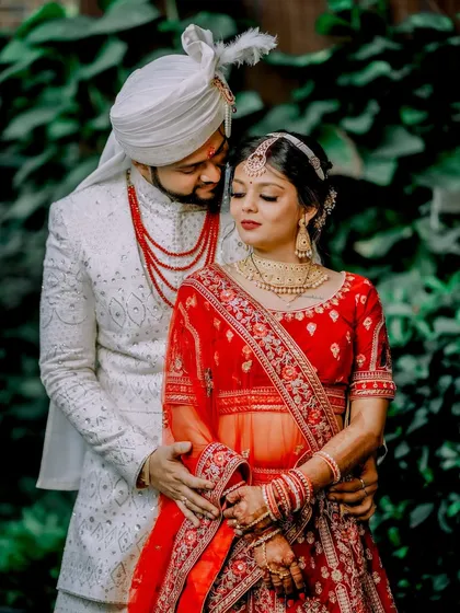 A beautiful outdoor portrait of the bride and groom. Her red lehenga and his white sherwani create a striking contrast, making for a classic and elegant wedding photo.