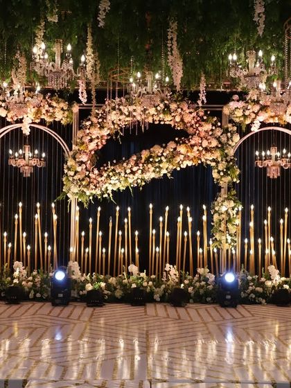 A breathtaking reception stage with a canopy of hanging greenery and chandeliers. The backdrop features candle-lit arches and lush florals, creating an atmosphere of pure romance and enchantment.