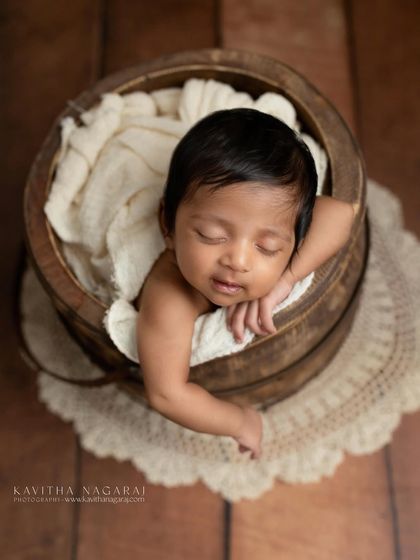 A two-month-old baby peeks over the edge of a rustic wooden bucket, showing that beautiful portraits are possible even after the first few weeks. That little smirk is everything.