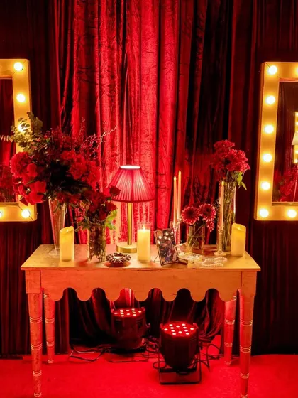 A detail shot of a decor vignette, featuring vanity mirrors with globe lights, tall candles, and deep red floral arrangements against a rich velvet curtain.