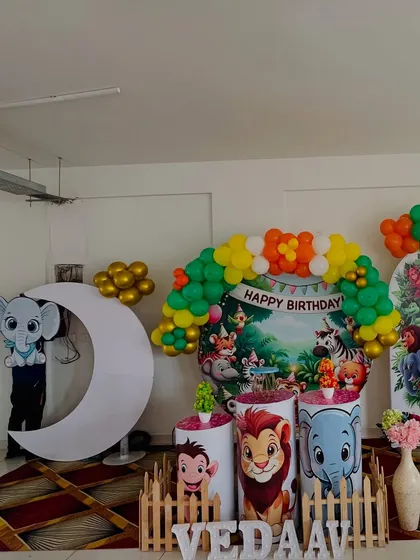 A classic jungle book style setup for a first birthday. It includes a circular backdrop with cartoon animals, character-themed pedestals, and a colorful balloon arch.