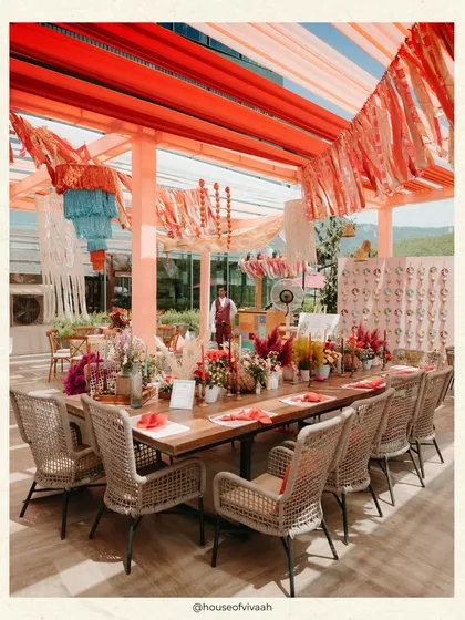 A long wooden community table at the Pahadi Mehendi, set under a canopy of rust-colored tassels and drapes, creating a warm and inviting space for guests to gather.