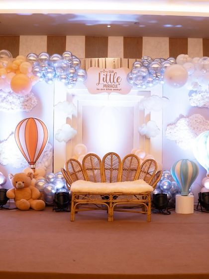 The main stage for the 'Our Little Miracle' baby shower. The setup features a beautiful rattan peacock chair set against a backdrop of soft clouds and hot air balloons.