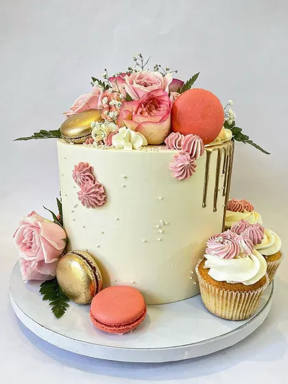 For a more sophisticated theme, I created this elegant floral cake. It's a smooth buttercream cake with a delicate gold drip, adorned with fresh pink roses, macarons, and paired with coordinating cupcakes for a complete, classy look.