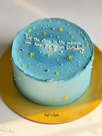 A dreamy birthday cake with a blue ombre buttercream base, decorated to look like a starry night sky with a hand-piped message.