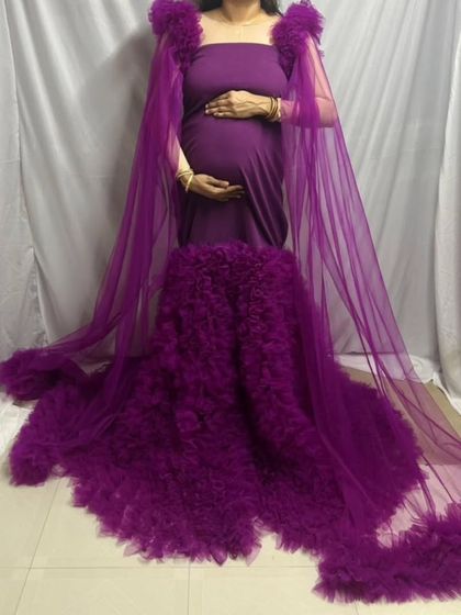 This deep purple maternity gown features a dramatic ruffled train and a sheer cape for a truly regal look. It's a statement piece perfect for a memorable pregnancy photoshoot.