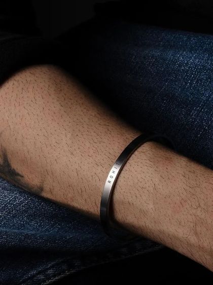A silver cuff bracelet engraved with 'ROWE', worn casually with denim. This shot shows the bracelet's effortless style.