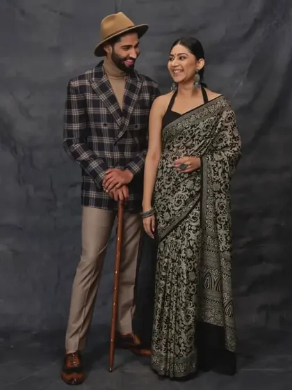 As featured in The Wedding Affair. This image from our magazine feature captures a timeless look, pairing a classic black floral saree with a contemporary checked blazer and fedora, illustrating our versatile styling.