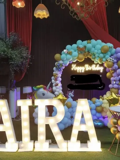 A unicorn-themed birthday party on a stage. This decoration includes large marquee letters, a circular balloon arch, and unicorn props.