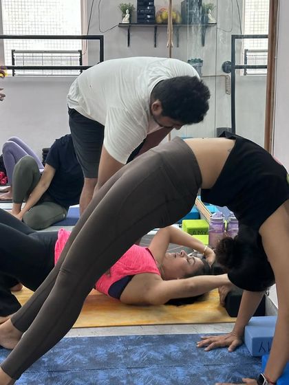 A student working on her wheel pose against the wall during a backbend intensive. The wall provides support and a target, helping to deepen the pose safely with correct alignment.