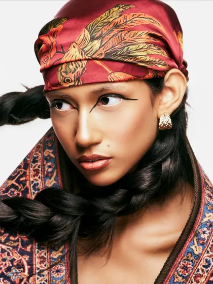 A close-up on the details. The sharp, graphic winged eyeliner is the centerpiece, complemented by a thick, structured braid and a patterned headscarf for a fusion of tradition and high fashion.