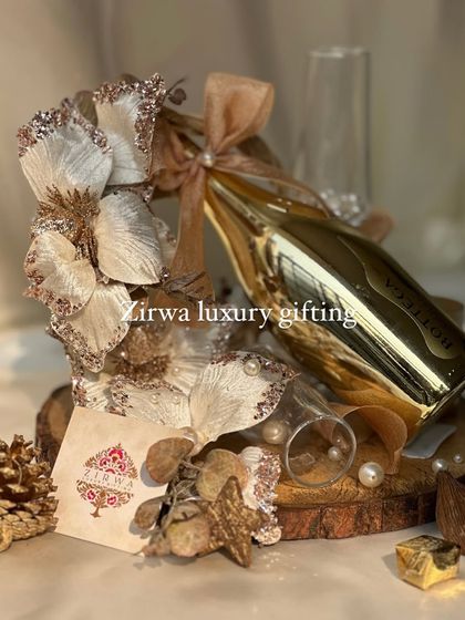 A touch of gold for the Christmas season. This arrangement features a golden bottle of sparkling wine, two champagne flutes, and glittering floral decorations on a wooden base.