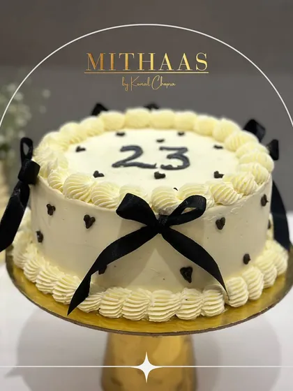 A classic and elegant 23rd birthday cake. The white frosting is decorated with delicate black ribbon bows and tiny black hearts, creating a chic and timeless look.