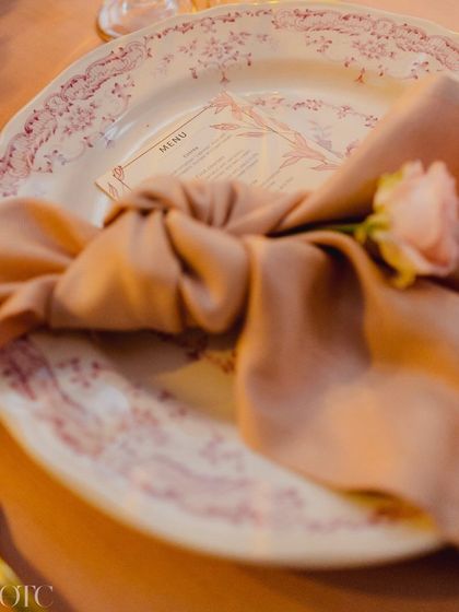 A close-up of the table setting for a reception dinner in Lake Como, featuring vintage-style plates and a beautifully tied napkin with a single pink rose.
