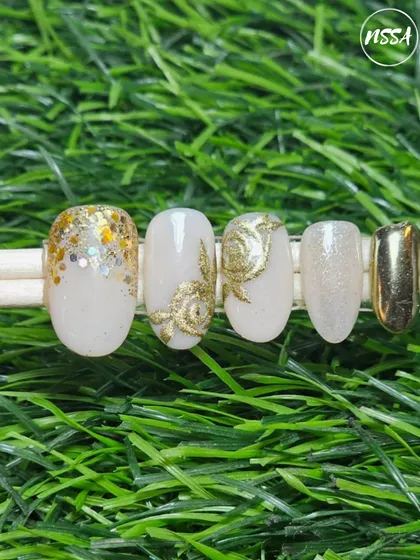 This elegant nail set combines multiple gold techniques. It features a full chrome nail, gold leaf accents, glitter fade, and textured gold floral art, all on a soft, milky white base.