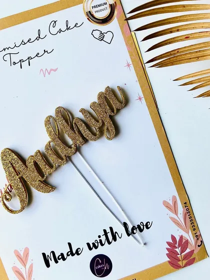 A close-up of the "Aadhya" gold glitter topper on its packaging, highlighting the texture and sparkle.