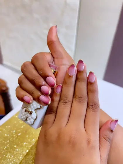 Holding a bottle of polish, this shot gives a great view of the pink ombre nails with glittery tips. The oval shape of the nails enhances the elegance of the color gradient.