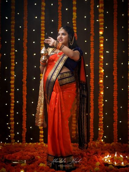 A festive and vibrant portrait celebrating tradition. The mother-to-be, dressed in a stunning orange saree, is surrounded by a curtain of marigolds and diyas, creating a truly magical atmosphere.
