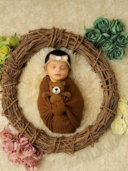 A sleeping newborn is nestled within a rustic grapevine wreath, holding a tiny teddy bear. The contrast of the natural textures and soft flowers creates a beautiful, earthy feel for this baby portrait.