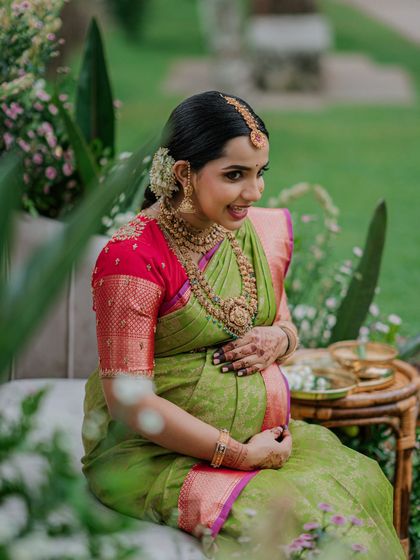 A serene moment from a Valaikappu photoshoot. The green and pink silk saree is draped to create a look of pure grace and maternal glow.