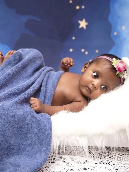 Even awake moments can be dreamy. This baby girl lies on a tiny bed under a soft blue blanket, looking curiously at her surroundings against the starry night sky.