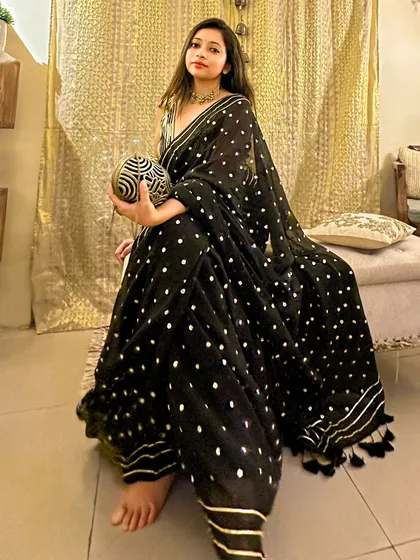 A full-length shot showing the beautiful fall of the black mul cotton saree. The fabric is light and comfortable, but the sequin and gota patti work make it festive enough for a wedding.